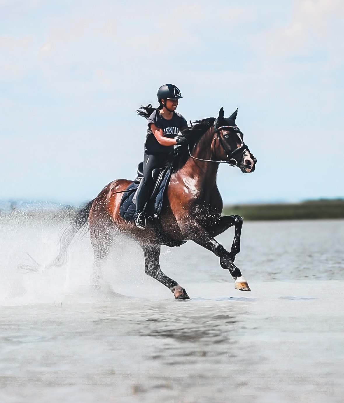 Rider cantering a bay horse through shallow water with an Equiveron saddle